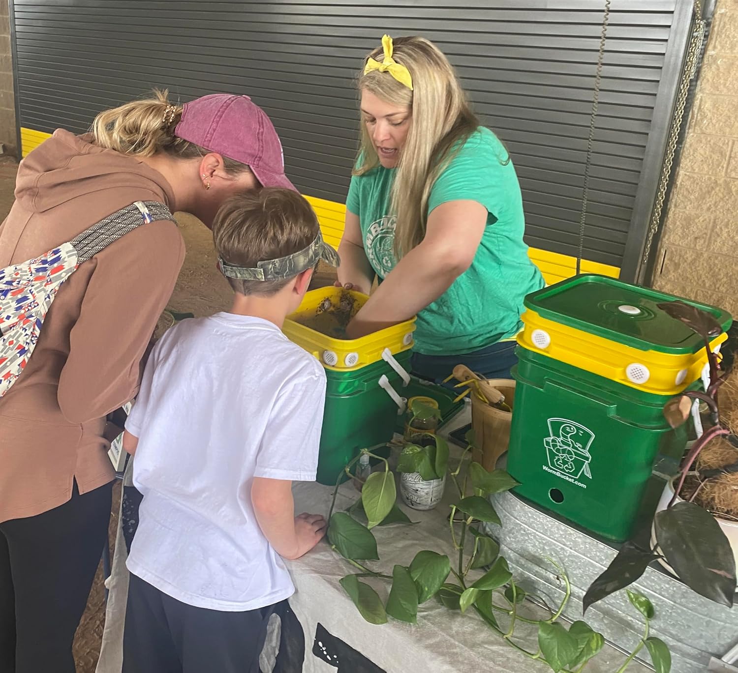 A teacher instructing a child on how to compost with worms using the worm bucket