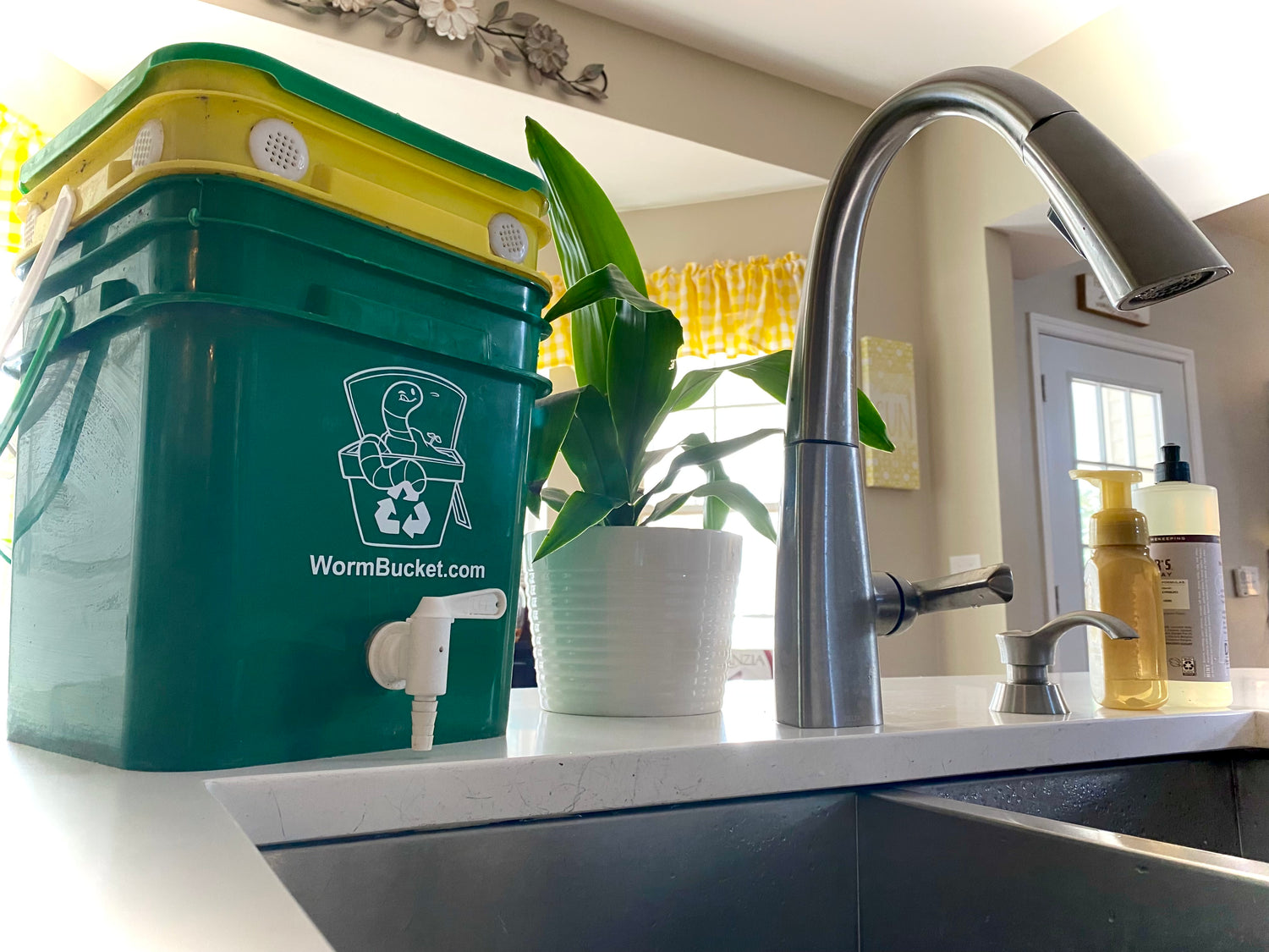 An image of a kitchen worm composter next to the sink. Worm Compost Bins are used for turning food scraps into an organic soil amendment called Worm Castings.